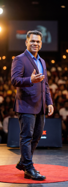 Shankar J on a red stage circle in front of a full auditorium, 728 by 2000 pixels